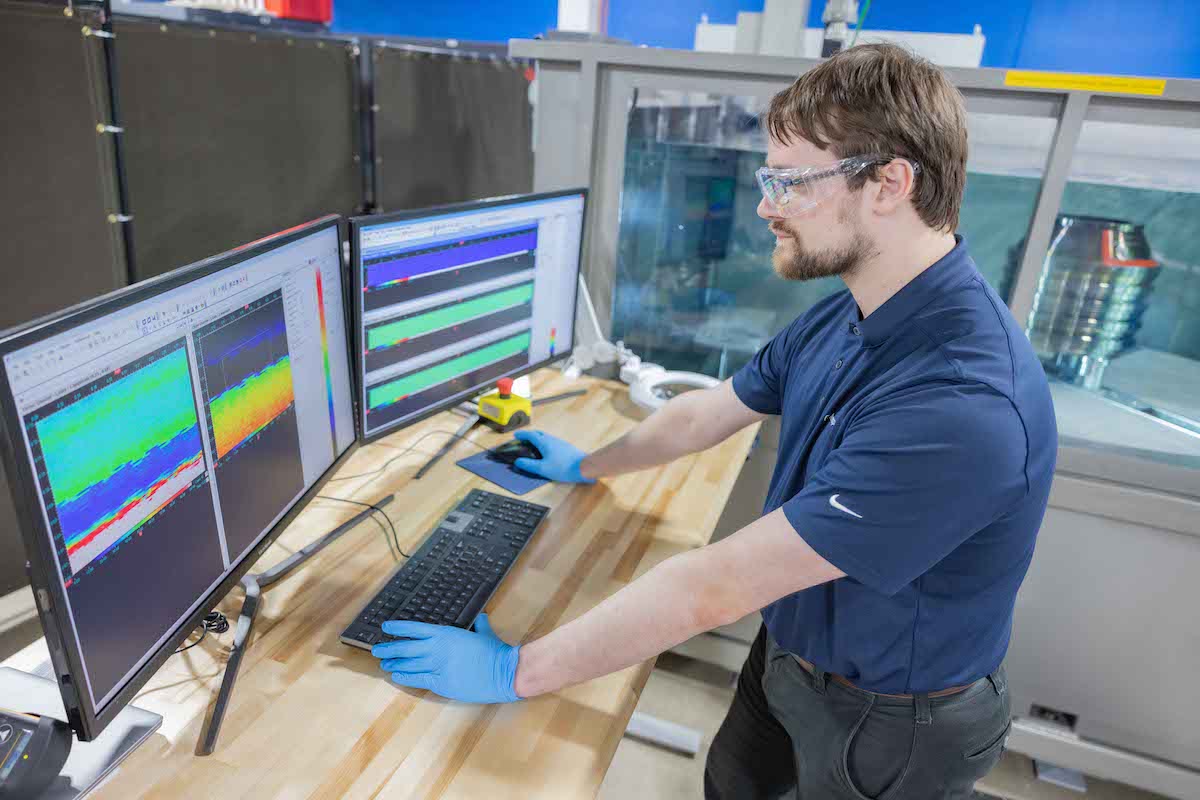 Nick Van Zandt, an AIS Lead Engineer, studies the scan of an engine part submerged in an ultrasonic immersion tank